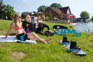 Wakeboarderinnen entspannen und sonnen sich auf der Liegewiese am See in Süsel neben der Seeterrasse und dem Backsteinhaus mit dem Bistro