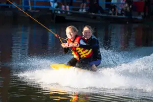 Zwei strahlende Mädchen knien auf dem Kneeboard bei voller Fahrt und spritzendem Wasser in Süsel Seeparx