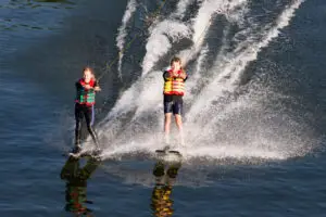 Zwei Kinder beim Wasserski Fahren nebeneinander auf dem See im Sonnenlicht