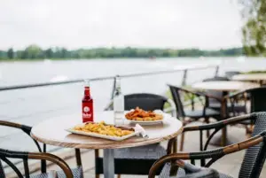 Pommes und Getränke stehen auf einem Tisch des Bistros auf der Sonnenterrasse mit Blick über den See in Süsel Seeparx