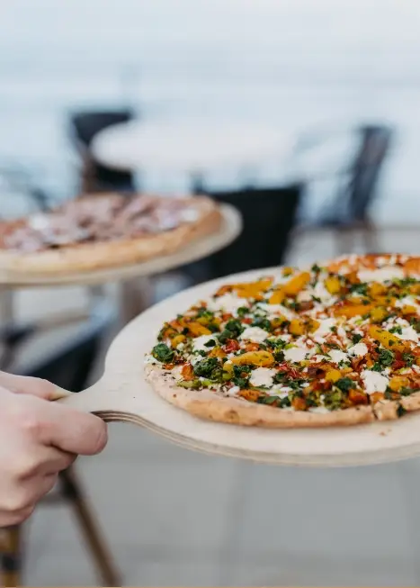 Knusprige und reich belegte Pizzen werden von einem Mitarbeiter des Süsel Seeparx Teams auf der Sonnenterrasse serviert