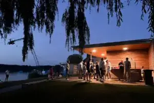 Menschen grillen in Süsel Seeparx vor dem überdachten beleuchteten Holzhaus in der Abenddämmerung