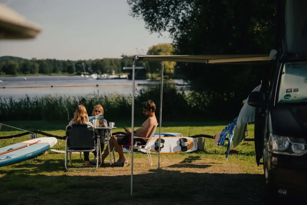Camper sitzen gemütlich in der Sonne am Seeufer auf Gartenmöbeln in Süsel Seeparx